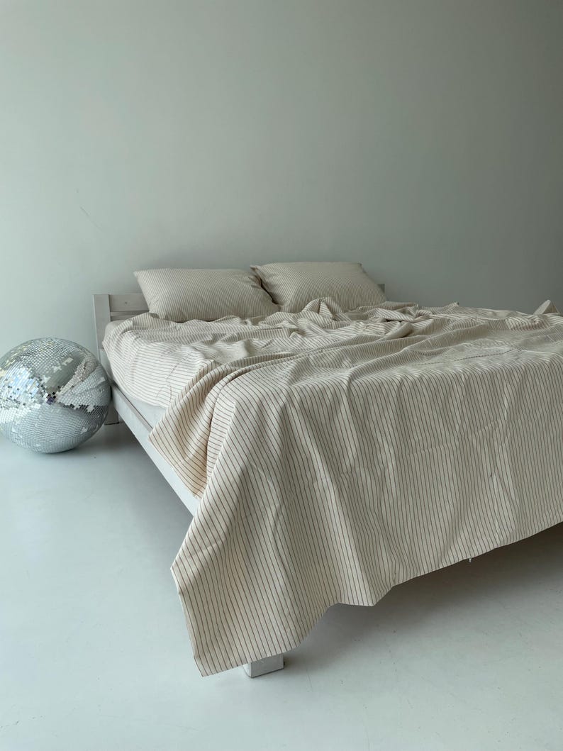 a bed with a striped blanket and pillows, along with a silver disco ball on the floor next to the bed.