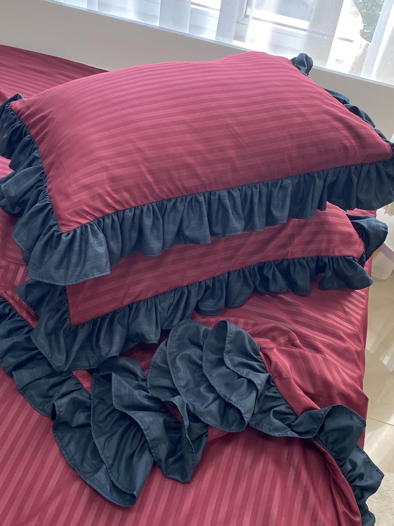 a bed with a red and black striped comforter and matching pillows with ruffled edges.