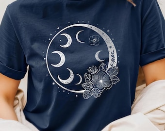 Op de afbeelding: Marineblauwe t-shirt met een wit maansikkels ontwerp, fasen, sterren en bloemaccenten. De afbeelding is gecentreerd, waardoor een hemels en botanisch thema ontstaat. De mouwen zijn opgerold.