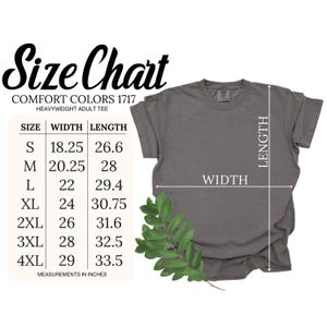 K&ouml;nnte beinhalten: Ein graues Comfort Colors Heavyweight-Erwachsenen-T-Shirt mit einer Gr&ouml;&szlig;entabelle. Die Tabelle zeigt die Ma&szlig;e in Zoll f&uuml;r die Gr&ouml;&szlig;en S bis 4XL. Ein gr&uuml;ner, bl&auml;ttriger Zweig befindet sich am unteren Rand des Shirts.