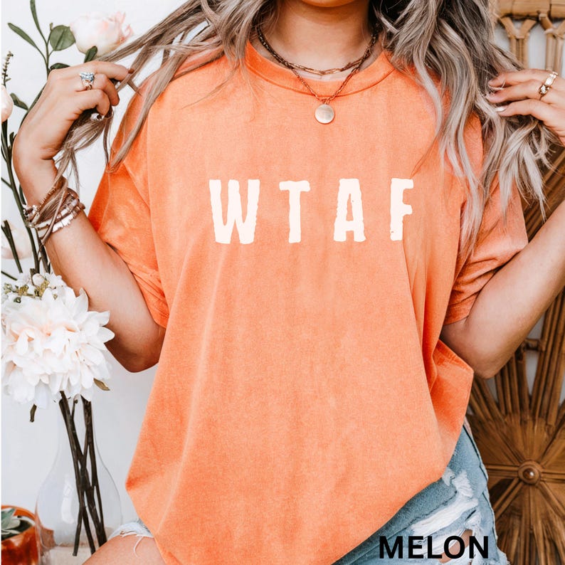 K&ouml;nnte beinhalten: Melonfarbenes T-Shirt mit den wei&szlig;en Buchstaben "WTAF" auf der Vorderseite. Das Shirt hat kurze &Auml;rmel und einen Rundhalsausschnitt. Das Wort "MELON" ist unten auf dem Shirt in Wei&szlig; aufgedruckt. Das Shirt besteht aus einem weichen Material.