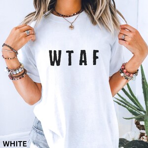 K&ouml;nnte beinhalten: Wei&szlig;es T-Shirt mit den schwarzen Buchstaben "WTAF" auf der Vorderseite. Das Shirt hat einen Rundhalsausschnitt und scheint aus einem weichen Material zu sein. Das Wort "WHITE" ist unten im Bild aufgedruckt.