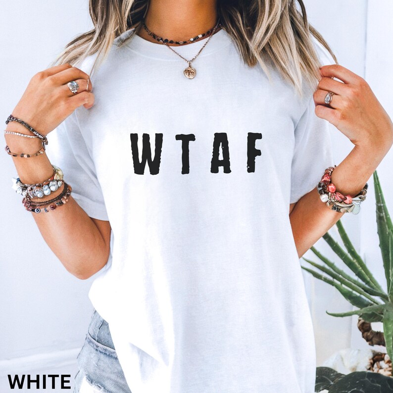 K&ouml;nnte beinhalten: Wei&szlig;es T-Shirt mit den schwarzen Buchstaben "WTAF" auf der Vorderseite. Das Shirt hat einen Rundhalsausschnitt und scheint aus einem weichen Material zu sein. Das Wort "WHITE" ist unten im Bild aufgedruckt.