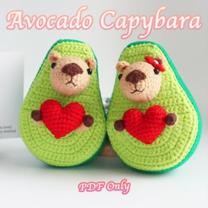 May include: Two crocheted avocado-shaped plushies with capybara faces holding red hearts. The plushies are green with brown eyes and noses. The text "Avocado Capybara" is at the top of the image and "PDF Only" is at the bottom.