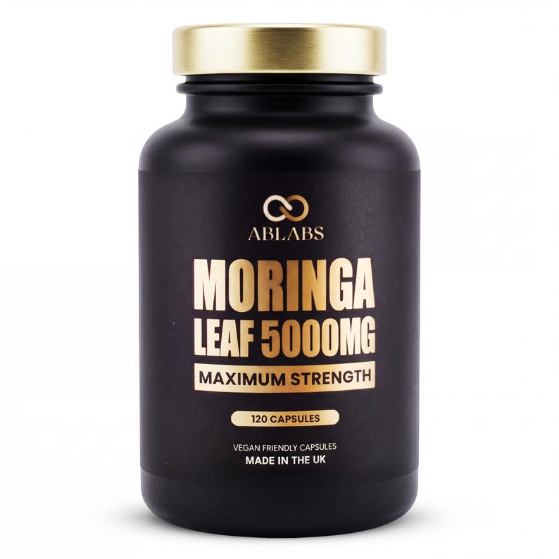 May include: A black supplement bottle with a gold lid. The label features the text "ABLABS MORINGA LEAF 5000MG MAXIMUM STRENGTH" in gold lettering. The bottle contains 120 capsules and is made in the UK.