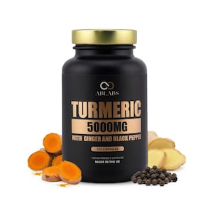 Może przedstawiać: Czarna butelka z suplementem ze złotą pokrywką, z napisem "TURMERIC 5000MG" z imbirem i czarnym pieprzem. Butelka zawiera 120 kapsułek i jest wyprodukowana w Wielkiej Brytanii. Pokrojony korzeń kurkumy, imbir i ziarna pieprzu otaczają butelkę.