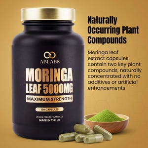 May include: A black bottle of Moringa Leaf 5000MG capsules with a gold lid. The label includes the text "Maximum Strength" and "120 Capsules". A small wooden bowl of green powder and several capsules are also visible.