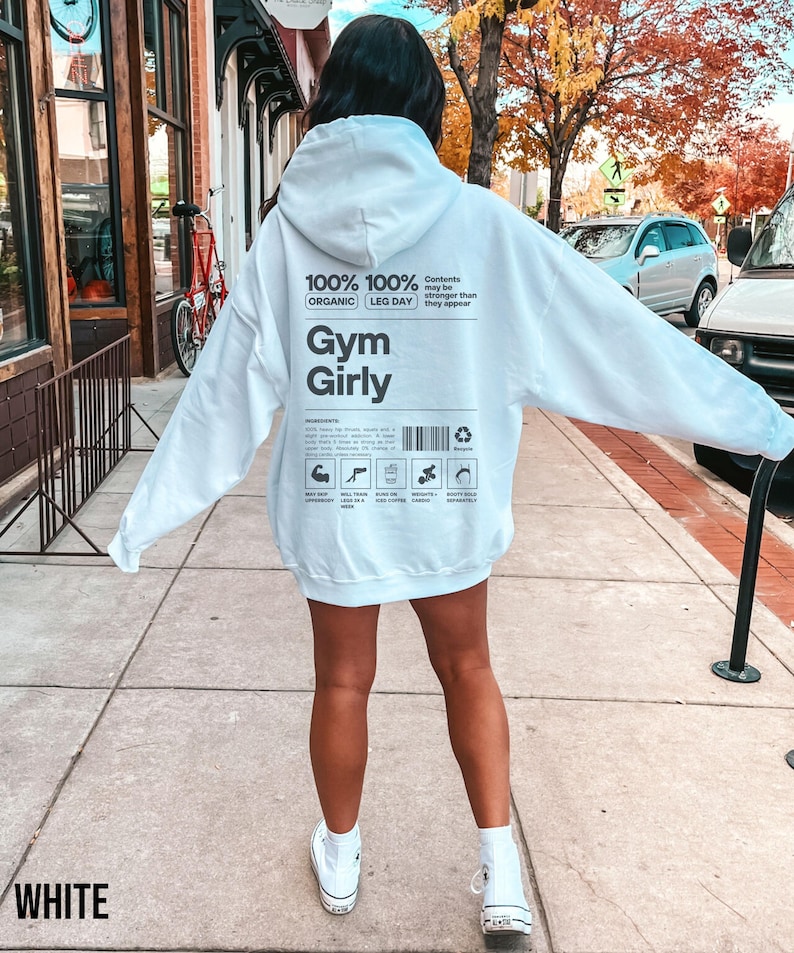May include: White hoodie with a black graphic print that says "100% Organic 100% Leg Day Gym Girly" and has a barcode and icons. The text "Contents may be stronger than they appear" is also printed on the hoodie.