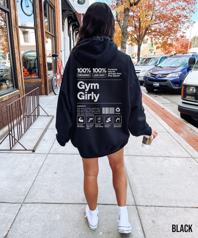 May include: Black hoodie with a white graphic that says "100% 100% Organic Leg Day Gym Girly" and includes a nutrition label with icons. The text "Contents may be stronger than they appear" is also included on the graphic.