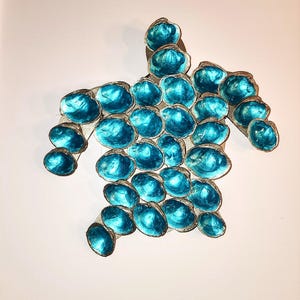 May include: A turquoise blue sea turtle wall art made of shells. The turtle is made of many small, round shells that are arranged in a pattern to form the shape of a turtle.