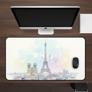 May include: A rectangular mousepad featuring a watercolor illustration of the Eiffel Tower and Notre Dame Cathedral in Paris, France. The design includes a colorful, pastel-like background. A black computer mouse sits to the right of the mousepad.
