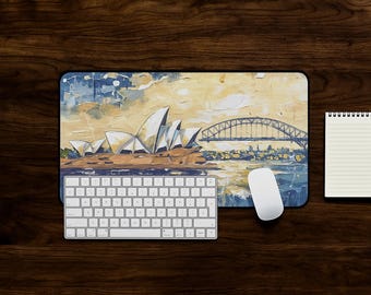 May include: A computer desk setup featuring a mousepad with an artistic depiction of the Sydney Opera House and Harbour Bridge. A white keyboard, mouse, and notepad are also present on a dark wood surface.