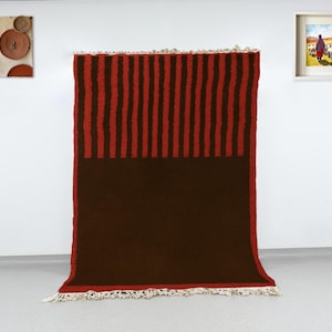 May include: A large, rectangular rug with a two-tone design. The top section features vertical red stripes against a dark brown background, while the lower section is solid dark brown. The rug has a fringed edge.
