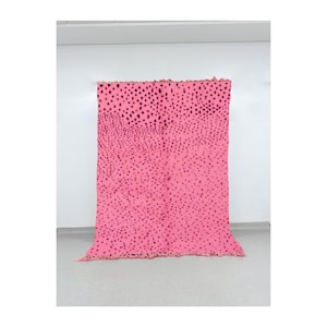 May include: A vibrant pink blanket with a pattern of dark purple dots. The blanket is rectangular, with a fringed edge along the bottom. The dots are densely packed at the top, fading towards the bottom.