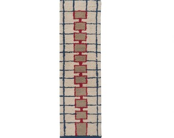 May include: A rectangular rug with a cream-colored background and a grid pattern in navy blue. The rug features a central column of alternating red and tan rectangular shapes. The edges are finished with a navy blue fringe.