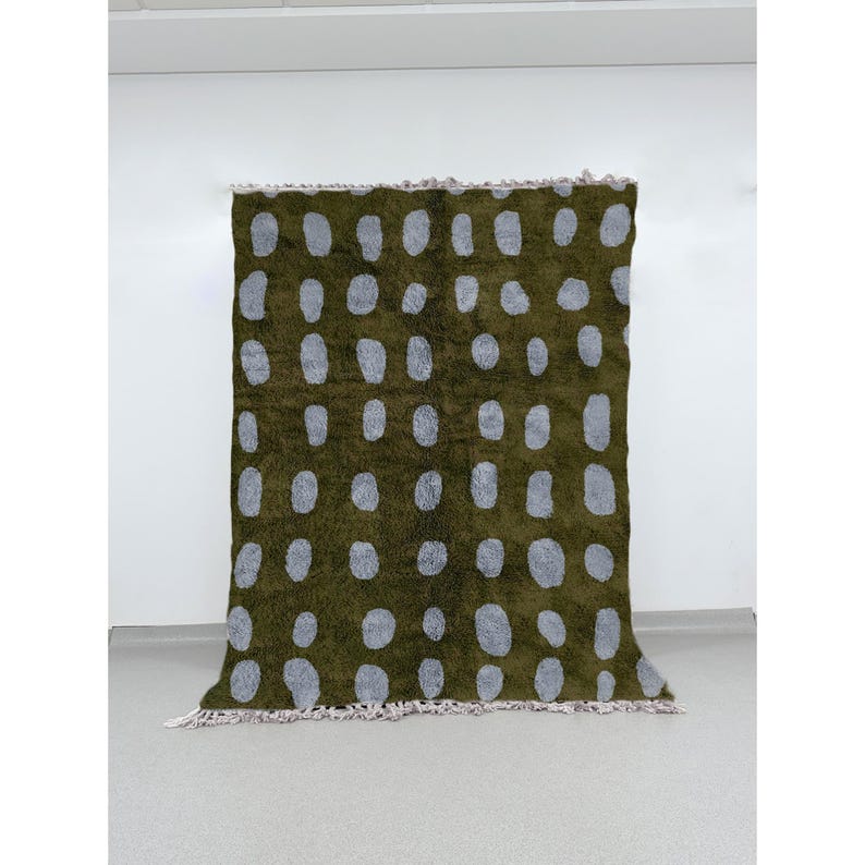 Handmade Moroccan Beni Ourain wool area rug in olive green with evenly spaced gray polka dots, woven by Berber artisans using traditional techniques. The shaggy wool texture adds warmth and softness, while the modern dotted pattern creates a playful yet minimalist vibe. Perfect for living rooms, bedrooms, or creative spaces seeking bold Moroccan flair and premium craftsmanship. This one-of-a-kind wool rug brings together artisanal skill, high quality, and contemporary design with tribal charm.