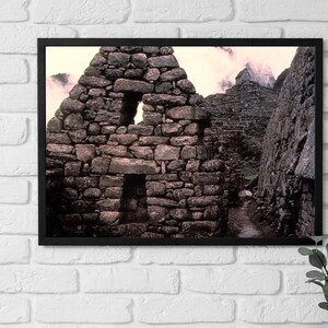 May include: A black and white photograph of a stone building with a triangular shape. The building has several windows and is surrounded by other stone structures.
