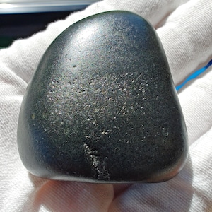 May include: A smooth, dark gray, oval-shaped rock with a slightly iridescent sheen.