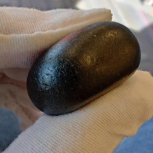 May include: A smooth, black, oval-shaped stone held in a white cloth.