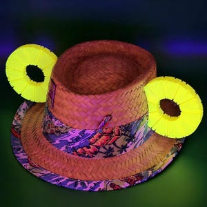 May include: A straw fedora hat with a patterned band featuring a tropical design. Two bright yellow, ring-shaped decorations, resembling pineapple slices, are positioned on either side of the hat. The hat is set against a dark green background.
