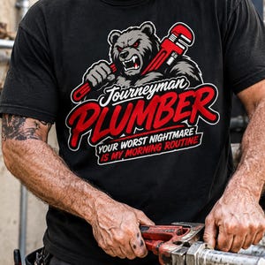 Könnte beinhalten: Schwarzes T-Shirt mit einer Grafik eines Bären, der einen roten Schraubenschlüssel hält, mit den Worten "Journeyman PLUMBER" in Rot und Weiß und dem Satz "YOUR WORST NIGHTMARE IS MY MORNING ROUTINE".