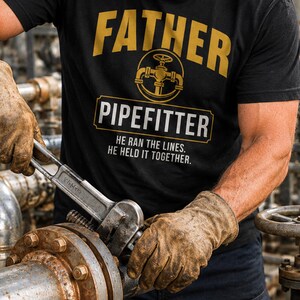 以下が含まれることがあります： 「FATHER PIPEFITTER」のゴールド文字と配管継手のグラフィックが特徴の黒いTシャツ。「HE RAN THE LINES. HE HELD IT TOGETHER.」の文字も含まれています。人がパイプにレンチを使用しています。