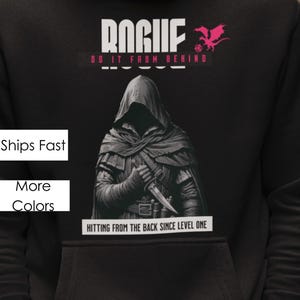Puede incluir: Figura negra con capucha sosteniendo una daga con el texto "ROGUE DO IT FROM BEHIND" y un gráfico de dragón rosa. El texto "HITTING FROM THE BACK SINCE LEVEL ONE" está debajo de la figura.
