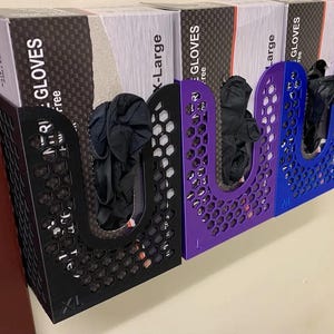 以下が含まれることがあります： 壁掛け式のグローブディスペンサーが3つあり、それぞれサイズラベルが異なります。XL、Large、Medium。ディスペンサーは、ハニカム模様の黒と紫のプラスチック製です。各ディスペンサーには、グローブの箱が入っています。