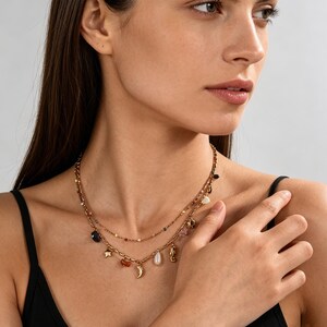 May include: A gold-coloured layered necklace with various charms, including a star, moon, seahorse, and teardrop-shaped pendants. The necklace also features small, colourful beads and gemstones. The woman is wearing a black vest top.
