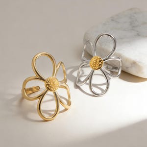 May include: Two adjustable rings shaped like open-petal flowers. One ring is gold-toned with a textured, circular center, and the other is silver-toned with a matching textured, gold-toned circular center. Both feature thin, wire-like petals.