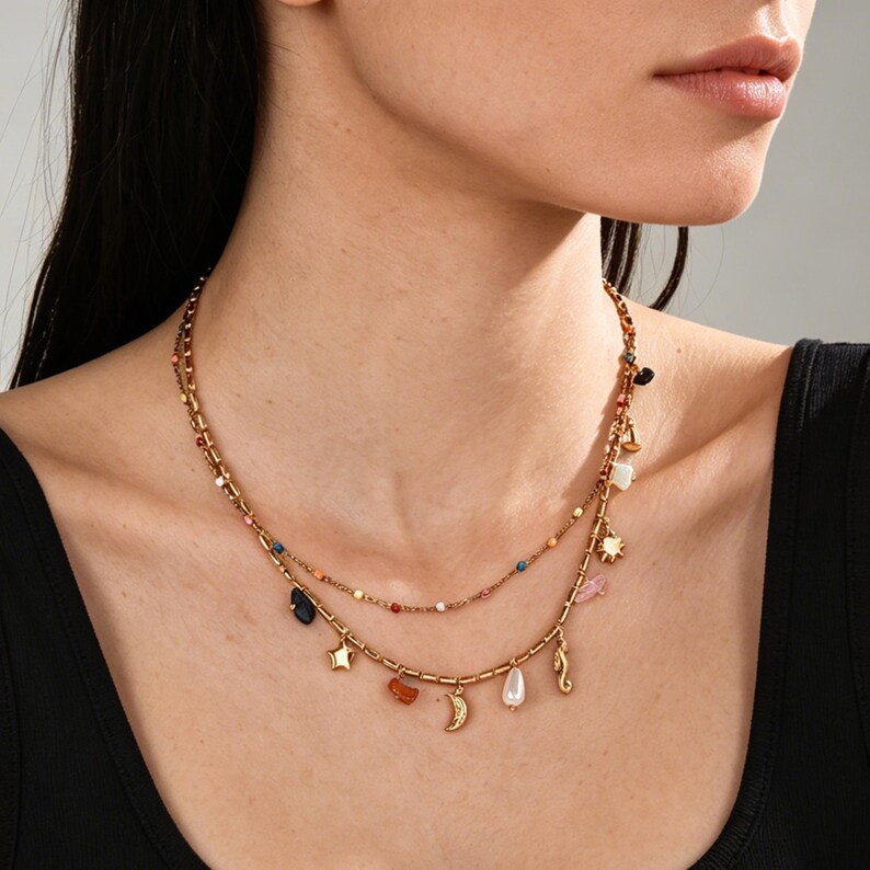 May include: Gold-coloured layered necklace with colourful beads and charms. The necklace features a star, moon, and other decorative charms. The model is wearing a black top.
