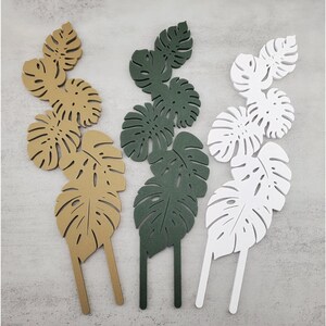 Tan, Green, and White six-leaf monstera trellis garden stakes on a grey background.