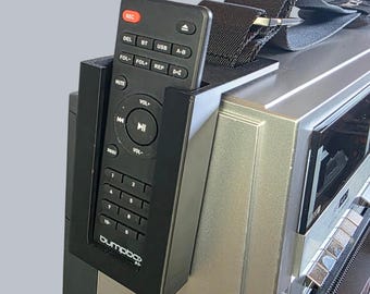 May include: A black plastic remote control holder mounted to the side of a silver boombox. The remote features a red record button, numeric keypad, and playback controls with the brand name bumpbox printed in white at the bottom of the remote.