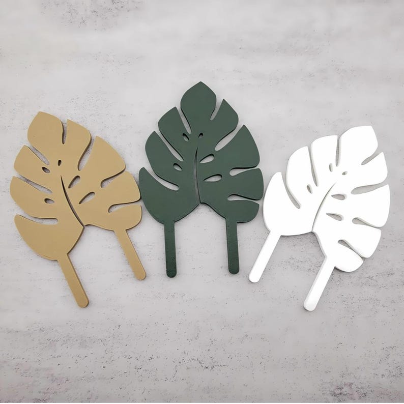 Tan, Green, and White single leaf monstera trellis garden stakes on a grey background.