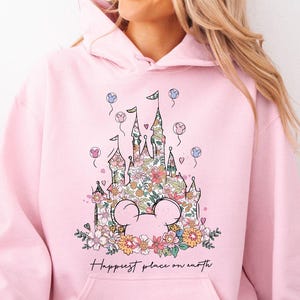 May include: A light pink hoodie with a floral design of a castle and the text "Happiest place on earth".