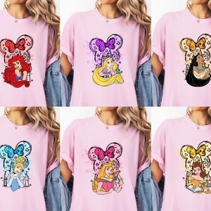 Puede incluir: Camisetas rosas con dise&ntilde;os de princesas Disney. Cada camiseta tiene un dise&ntilde;o en forma de Mickey Mouse con una imagen de princesa. Las princesas incluyen Ariel, Rapunzel, Pocahontas, Cenicienta, Aurora y Bella. Los dise&ntilde;os tienen acentos coloridos.