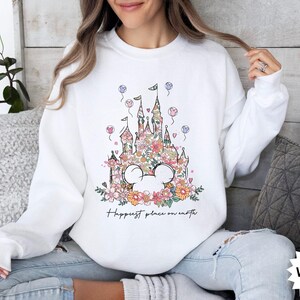 May include: White sweatshirt with a floral design of Cinderella's castle and the text "Happiest place on earth".