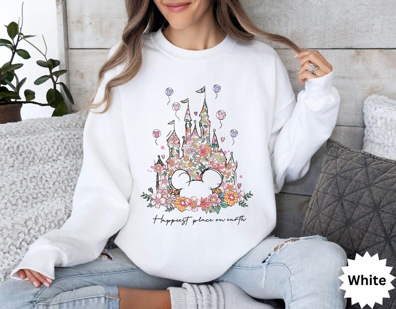 May include: White sweatshirt with a floral design of Cinderella's castle and the text "Happiest place on earth".