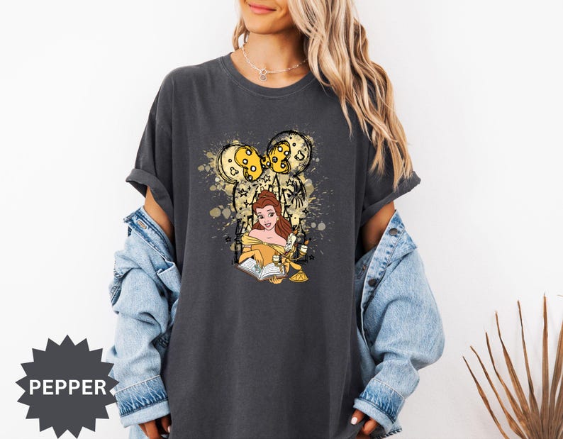 Puede incluir: Camiseta gris oscuro con un dise&ntilde;o de Bella de La Bella y la Bestia leyendo un libro, con un dise&ntilde;o inspirado en Mickey Mouse en oro y amarillo. La camiseta tiene un corte holgado y mangas cortas.