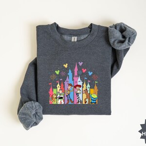 Peut inclure: Sweat-shirt gris fonc&eacute; avec un motif color&eacute; d'un ch&acirc;teau et de personnages de dessins anim&eacute;s. Le motif comprend un ch&acirc;teau avec des feux d'artifice et plusieurs personnages de dessins anim&eacute;s. Le sweat-shirt a des manches longues et un col rond.