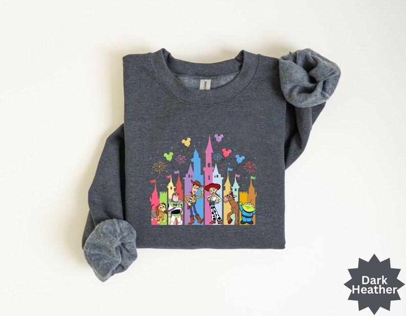 Peut inclure: Sweat-shirt gris fonc&eacute; avec un motif color&eacute; d'un ch&acirc;teau et de personnages de dessins anim&eacute;s. Le motif comprend un ch&acirc;teau avec des feux d'artifice et plusieurs personnages de dessins anim&eacute;s. Le sweat-shirt a des manches longues et un col rond.