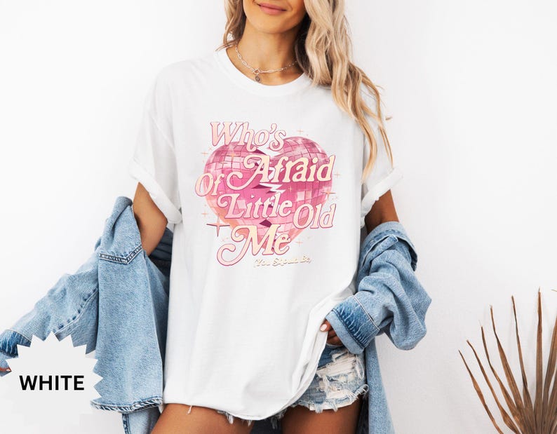 May include: White t-shirt with a pink graphic of a disco ball and the text "Who's Afraid of Little Old Me". The shirt is a relaxed fit and has short sleeves. A light blue denim jacket is draped over the shoulders.
