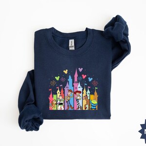 Peut inclure: Sweat-shirt bleu marine avec un motif color&eacute; repr&eacute;sentant un ch&acirc;teau et des personnages de dessins anim&eacute;s. Le motif comprend des personnages comme Woody et Buzz l'&Eacute;clair. Le sweat-shirt a un col rond et des manches longues.