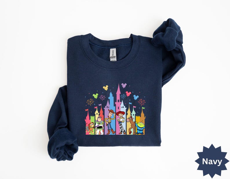 Peut inclure: Sweat-shirt bleu marine avec un motif color&eacute; repr&eacute;sentant un ch&acirc;teau et des personnages de dessins anim&eacute;s. Le motif comprend des personnages comme Woody et Buzz l'&Eacute;clair. Le sweat-shirt a un col rond et des manches longues.