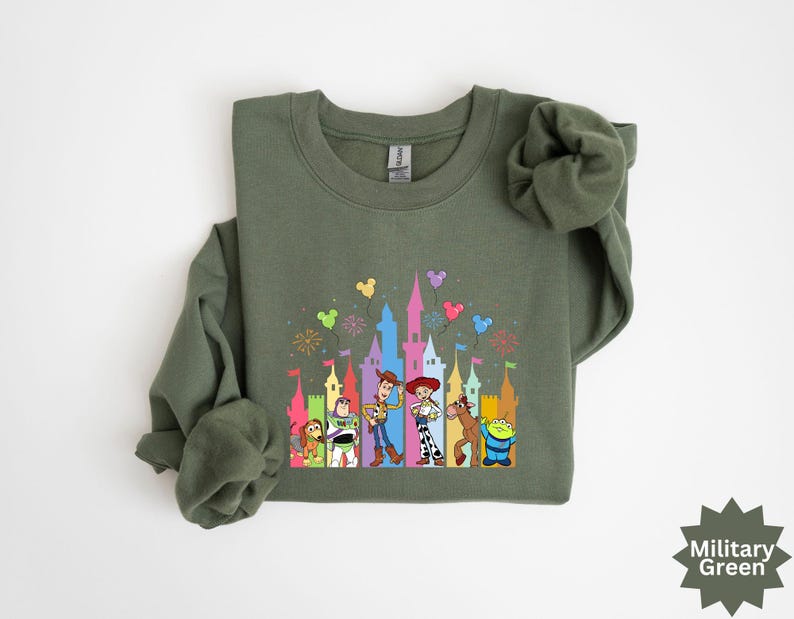 Peut inclure: Sweat-shirt vert militaire &agrave; col rond avec un graphisme color&eacute; de personnages de dessins anim&eacute;s devant un ch&acirc;teau. Le graphisme comprend des personnages comme Woody, Buzz l'&Eacute;clair, etc. Le sweat-shirt est en mati&egrave;re douce.