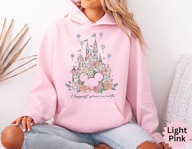 May include: A light pink hoodie with a floral design of a castle and the text "Happiest place on earth".