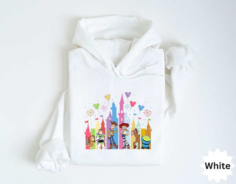 Peut inclure: Sweat-shirt &agrave; capuche blanc avec un graphisme color&eacute; de personnages de dessins anim&eacute;s et une silhouette de ch&acirc;teau. Le motif comprend des ballons et des feux d'artifice. Le mot "White" est dans le coin inf&eacute;rieur droit.