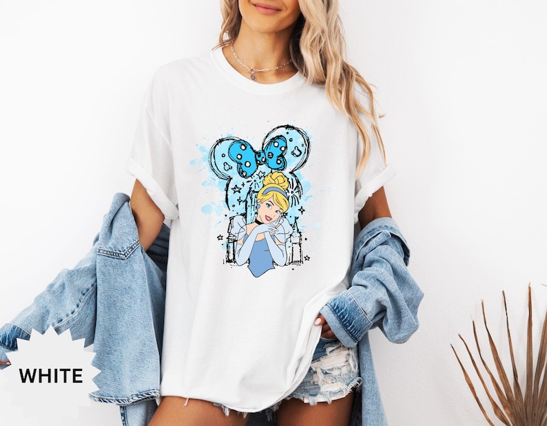 May include: White t-shirt with a blue and white illustration of Cinderella with a bow on her head and a castle in the background. The illustration is surrounded by stars and hearts.
