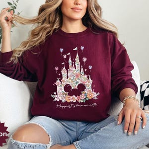 May include: A maroon sweatshirt with a floral print of Cinderella's castle and the text "Happiest place on earth".