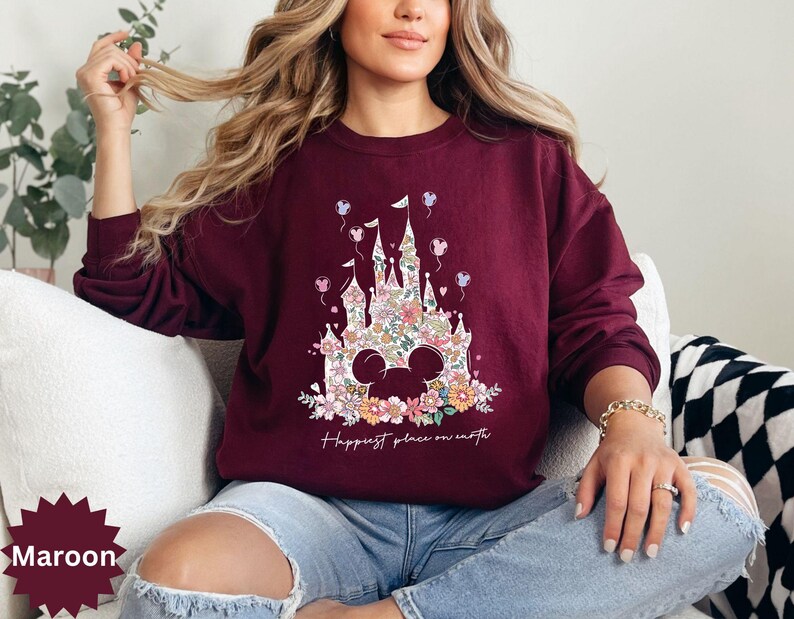 May include: A maroon sweatshirt with a floral print of Cinderella's castle and the text "Happiest place on earth".